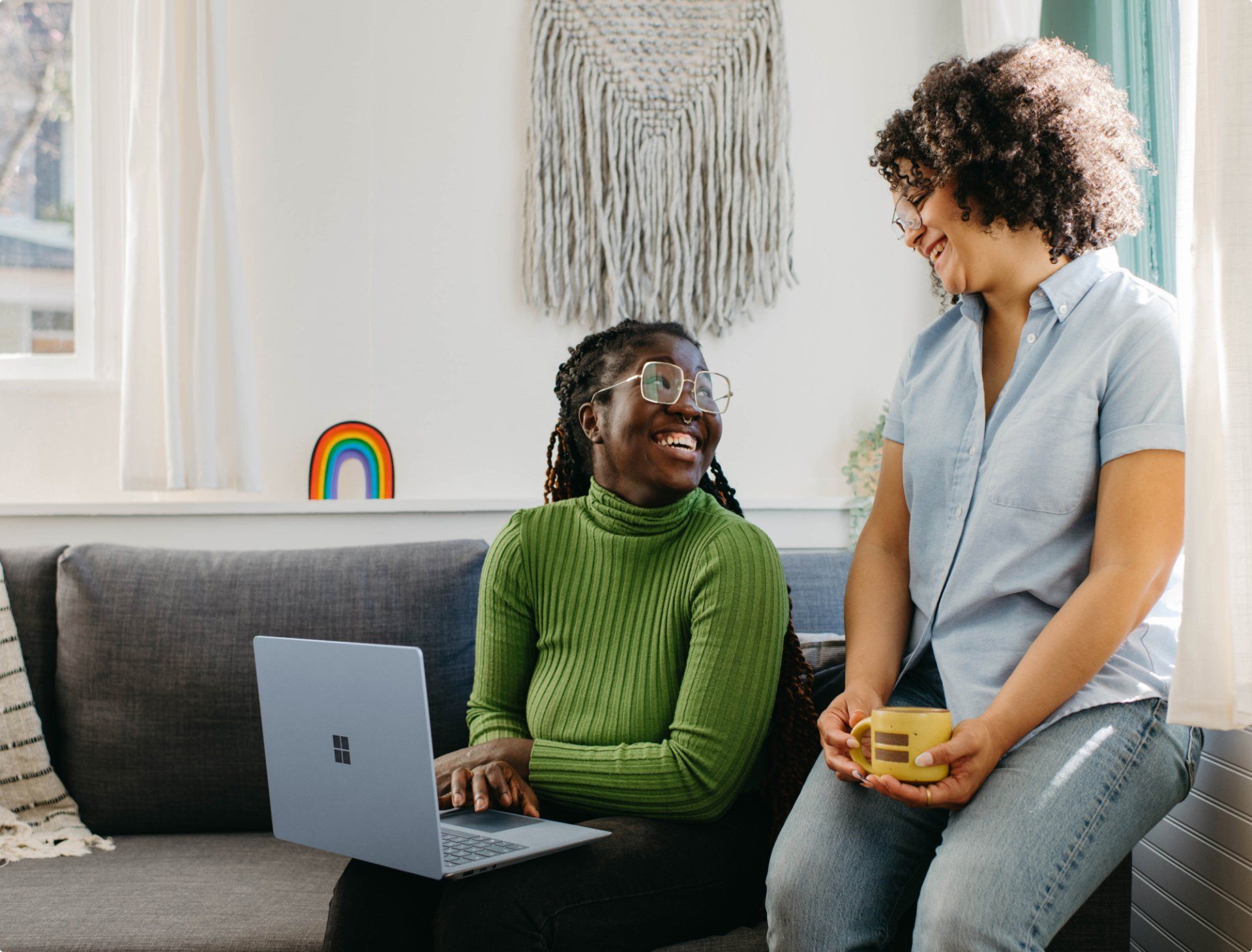 Two women are sitting on a couch with a laptop.